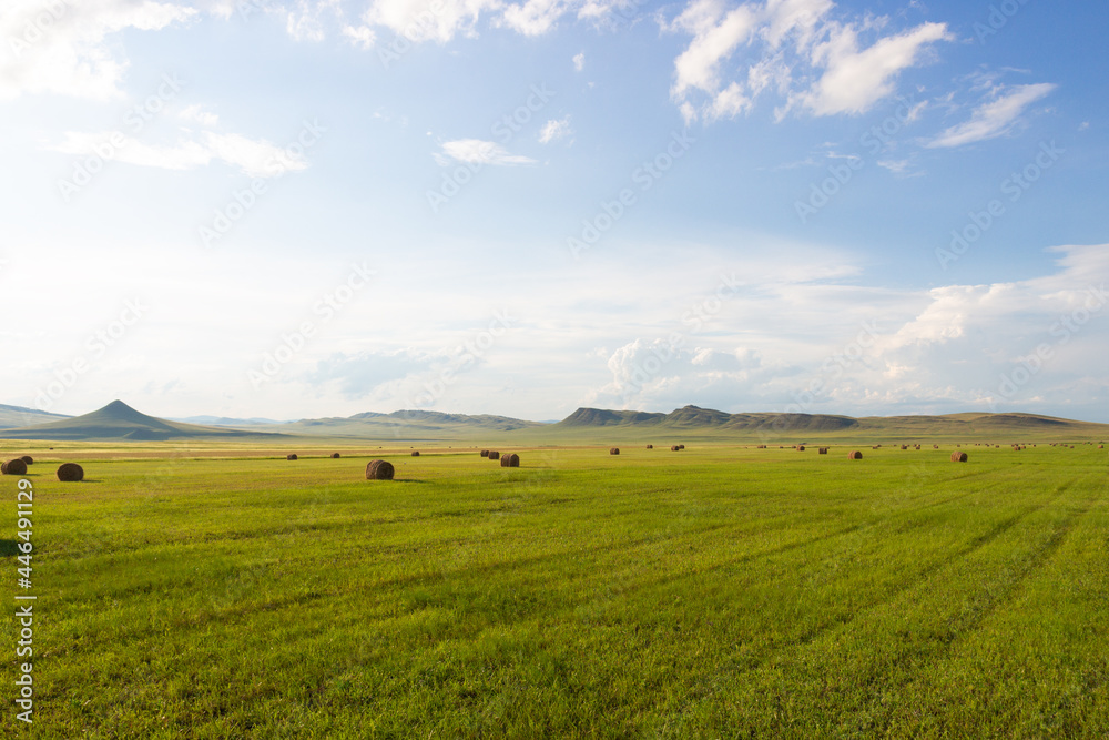 Summer landscape with hay bales on farming green fields against the background of cloudy sky and ridges of hills in Khakassia, Russia
