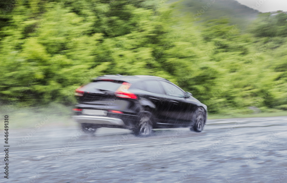 Fototapeta premium car moves under a downpour on a country road along the forest.