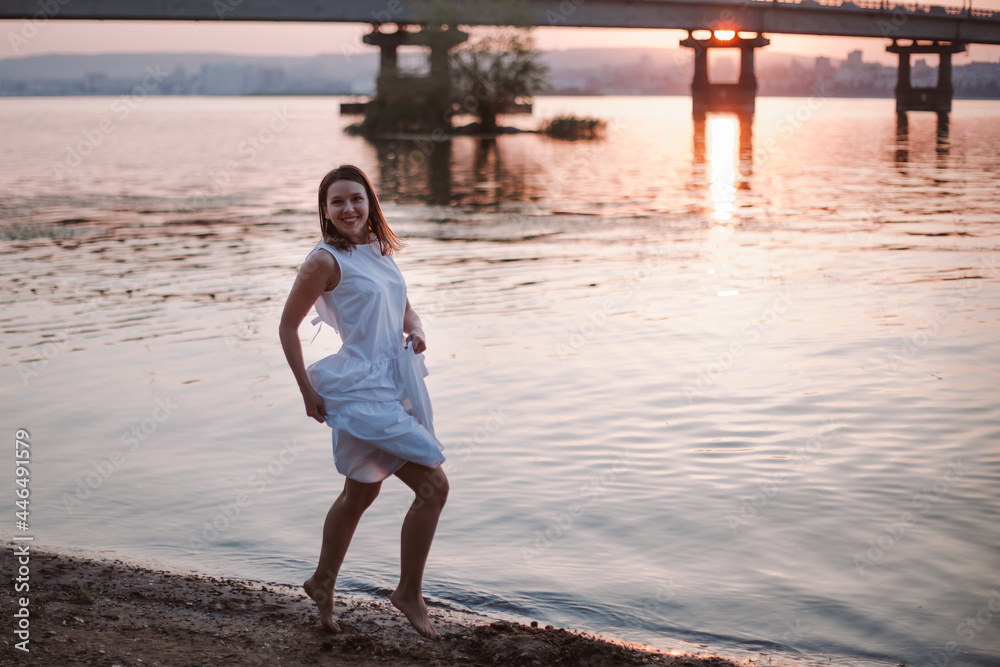Women jumping at sunset. A laughing, cheerful woman in a white summer dress is having a good time on the river beach at sunset on a summer evening. Women jumping at sunset. A laughing, cheerful woman in a white summer dress is having a good time on the river beach at sunset on a summer evening.