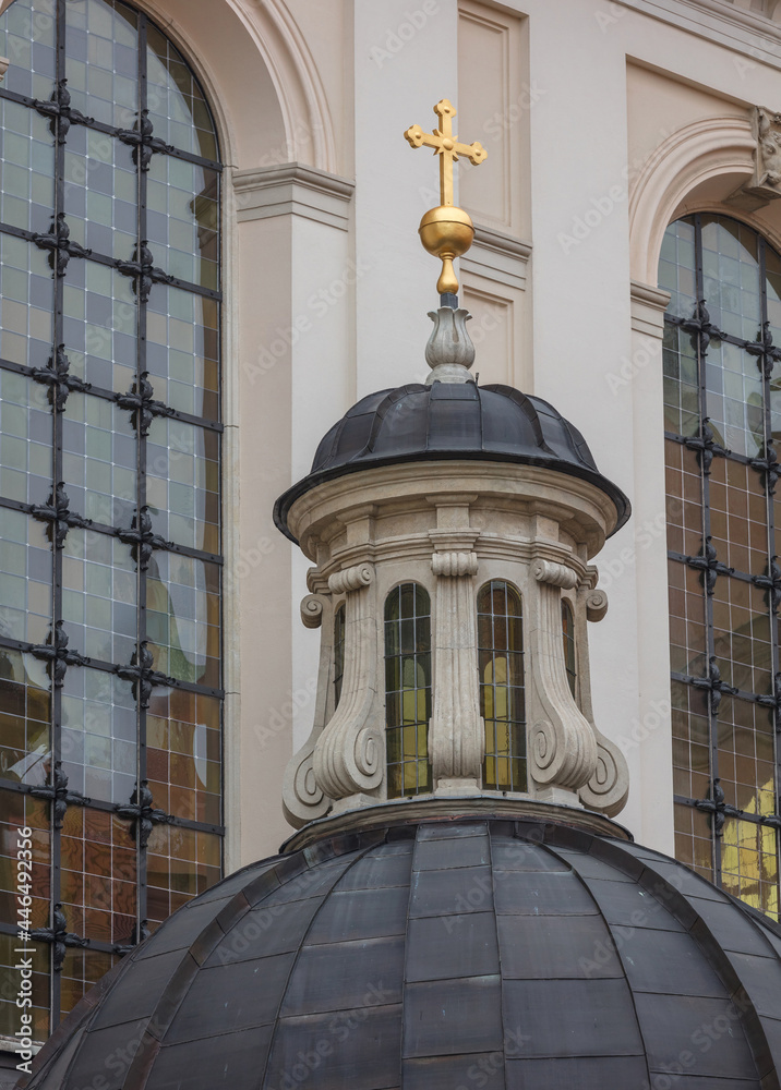 Close-up of the facade of an ancient building of the Catholic Church. Gold cross on a beautiful marble dome under a copper roof. In the background there are tall stained-glass windows.