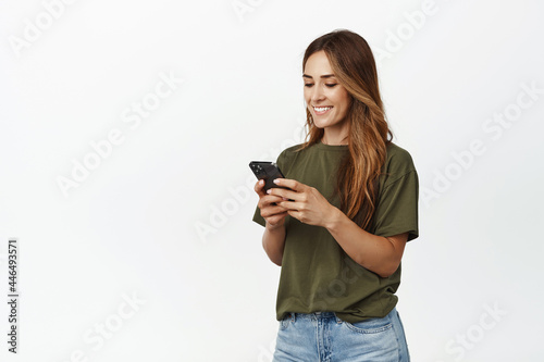 Image of smiling adult woman chatting in app, holding smartphone, looking at mobile phone screen happy, texting message, scroll shopping app, order smth in internet