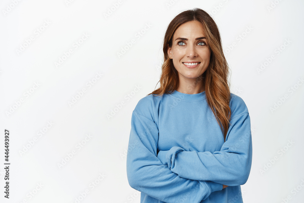 Image of confident and ambitious middle aged woman, cross arms on chest and looking aside with pleased determined smile, standing in blue shirt against white background Image of confident and ambitious middle aged woman, cross arms on chest and looking aside with pleased determined smile, standing in blue shirt against white background