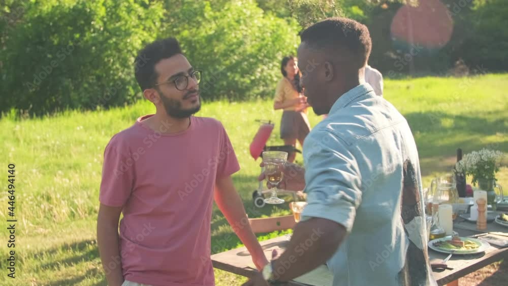 Modern young African American and Middle Eastern friends standing together in park chatting about something at party