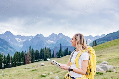 Smiling girl traveler with yellow backpack and paper map in the mountains.