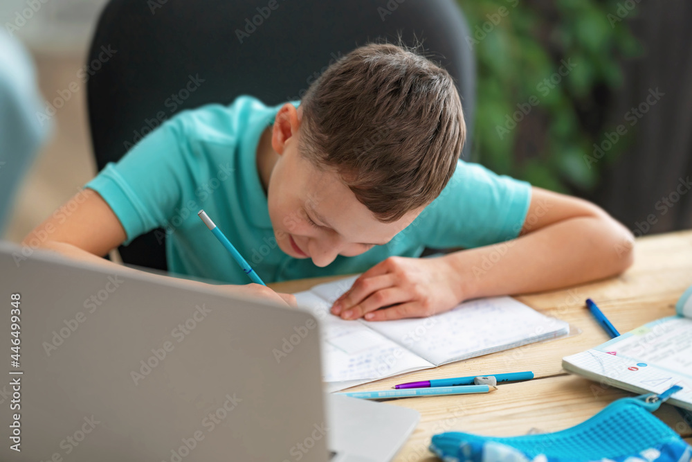 inquisitive boy uses laptop to study school subjects during his online lesson at home. Writing down topic lesson in notebook. E-Education Distance Home Education. inquisitive boy uses laptop to study school subjects during his online lesson at home. Writing down topic lesson in notebook. E-Education Distance Home Education.