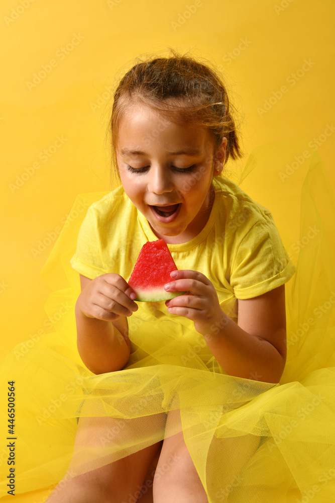 Happy caucasian girl holding a piece of watermelon she is going to eat with her hands. Yellow background with vertical copy space. Fresh and healthy fruit concept.