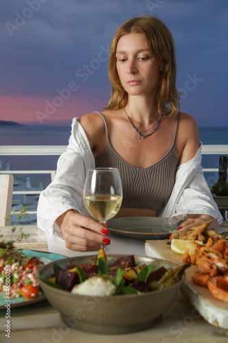  Young woman with white wine glass having dinner during sunset time. Relaxing summer vacation concept. © triocean