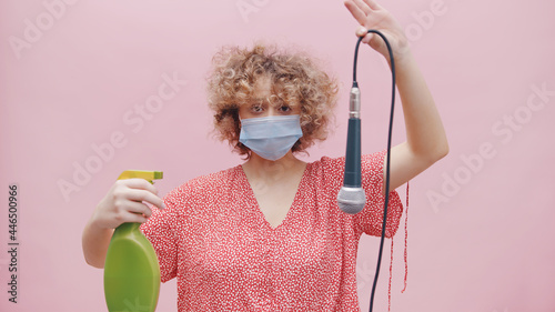 Girl wearing a face mask and a green spray bottle in her hand. Holding a mic upside down with its wire. Disinfecting the mic with disinfectant. Concept of sanitizing. Covid 19. Following Sops. photo