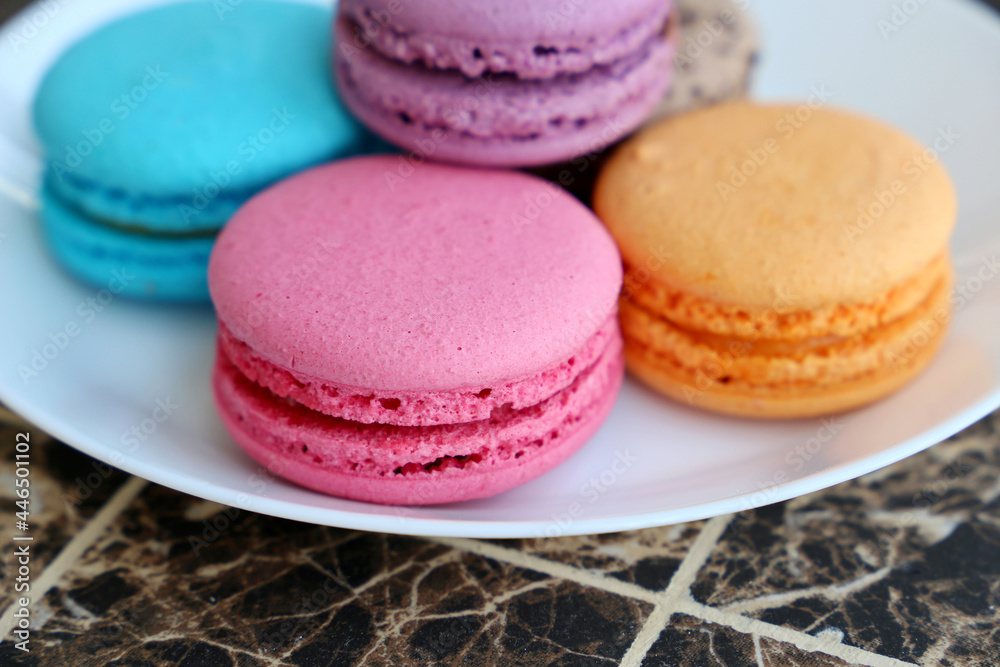 Macaroons in a white plate close up, colorful sweets. Strawberry, blueberry, vanilla and orange almond cookies with filling on a table Macaroons in a white plate close up, colorful sweets. Strawberry, blueberry, vanilla and orange almond cookies with filling on a table