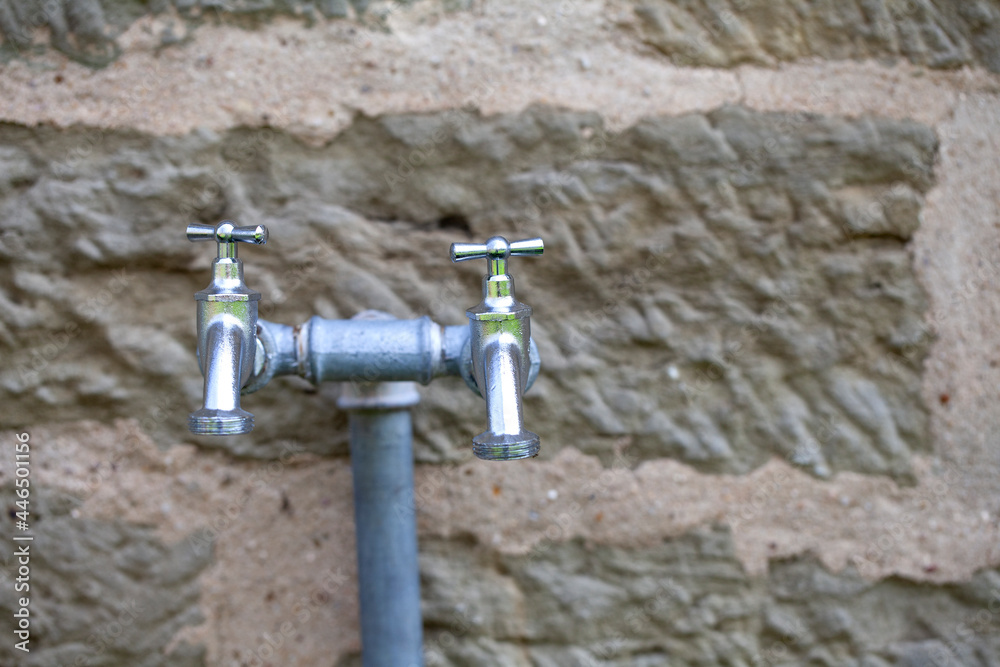 Outdoor double steel faucets in front of an old sandstone wall Outdoor double steel faucets in front of an old sandstone wall