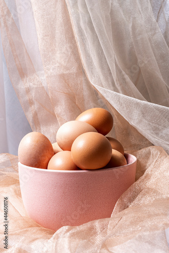 Pink bowl full of raw eggs surrounded by white and light brown tulle fabrics