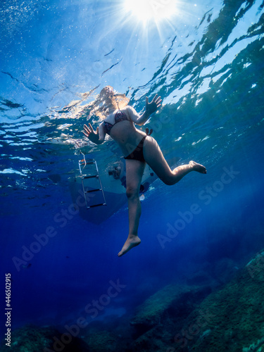 Young girl greets the photographer underwater. Young girl saying hello underwater with her hand.