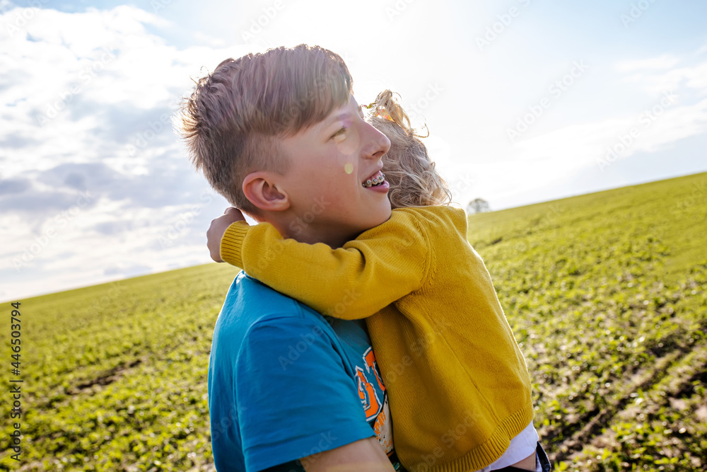 Brother and sister play outside. girl holds older brother by neck and