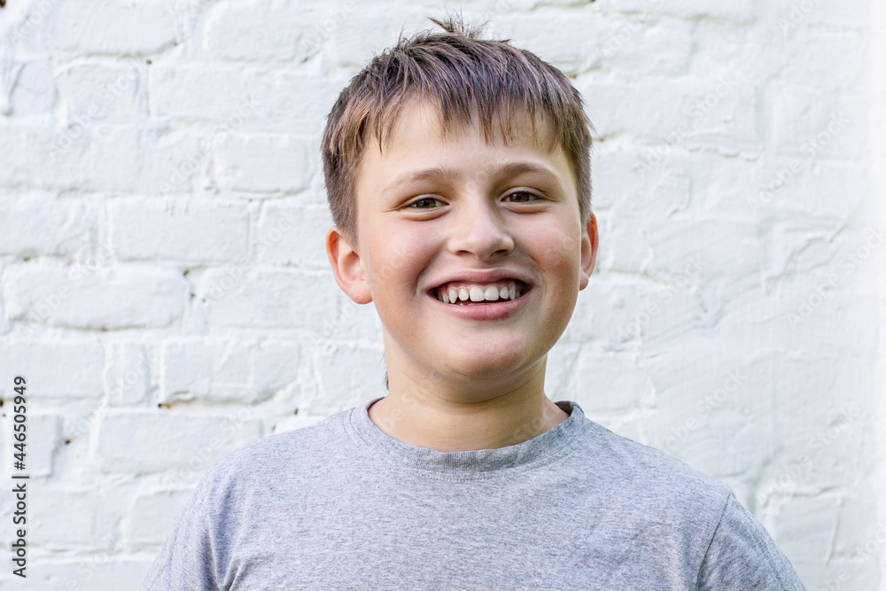 boy smiles happily. Portrait of amazing friendly little boy. handsome teenager near a white brick wall. boy smiles happily. Portrait of amazing friendly little boy. handsome teenager near a white brick wall.