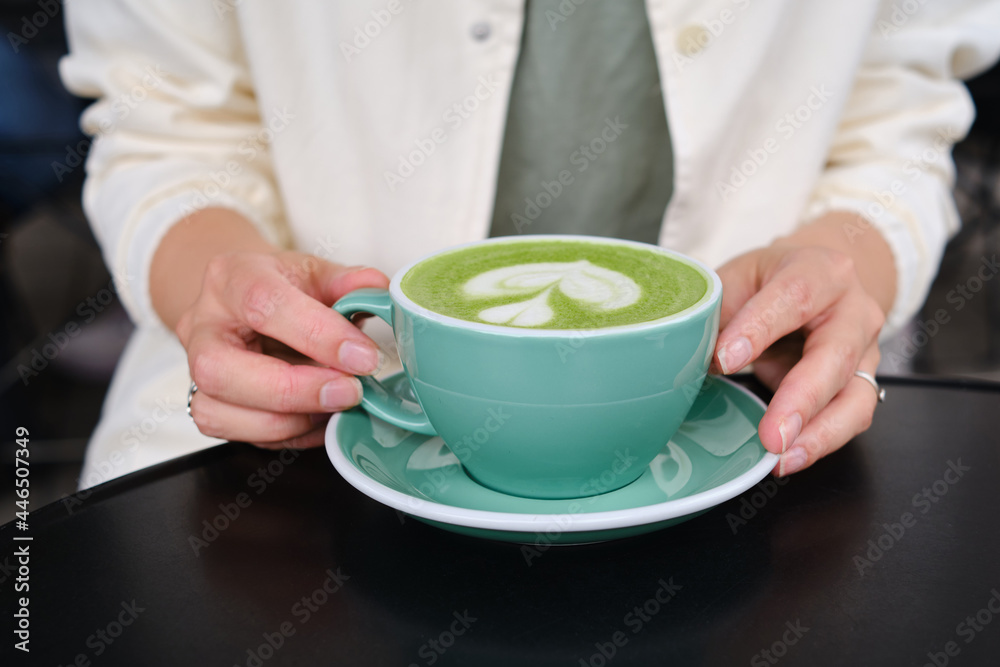 Woman with a cup of matcha latte sits on the summer terrace of a cafe. Delicious green matcha tea in a green cup close-up. Japanese hot milky beverage. Healthy Matcha Tea Made with Organic Ingredients Woman with a cup of matcha latte sits on the summer terrace of a cafe. Delicious green matcha tea in a green cup close-up. Japanese hot milky beverage. Healthy Matcha Tea Made with Organic Ingredients
