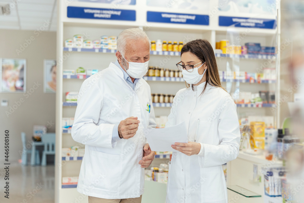 Obraz premium Colleague advice. Documentation and paper work in pharmacies during corona virus. A senior pharmacist explains the documentation in the pharmacy to a young pharmacist They wear uniforms and face masks