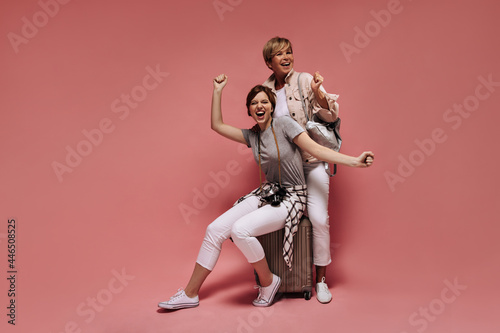 Emotional women with short cool hairstyle in white pants, t-shirts and light sneakers laughing on pink isolated background..