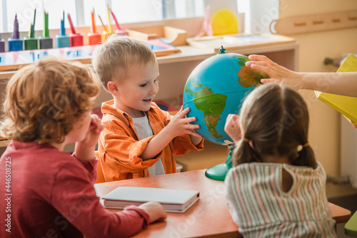 amazed boy looking at globe near blurred teacher and kids in montessori school photo