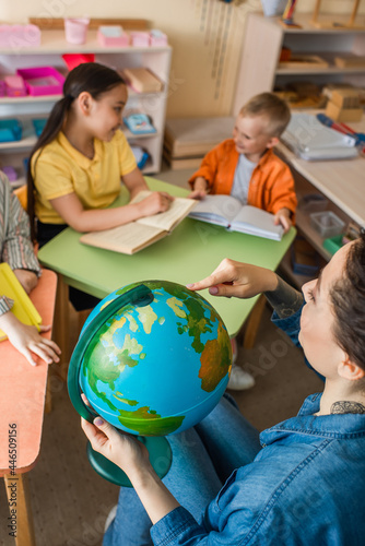 high angle view of teacher pointing at globe near multiethnic kids during lesson
