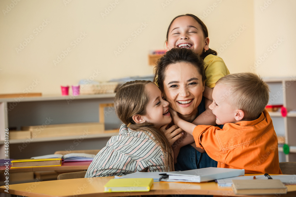 overjoyed multiethnic kids embracing happy teacher in montessori school