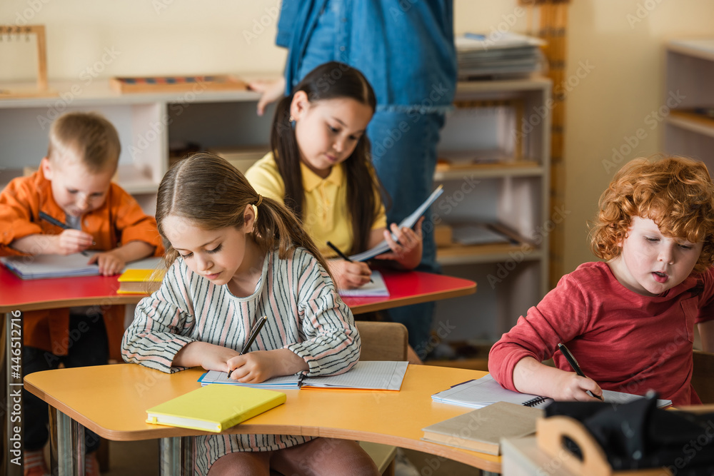 multiethnic children writing in notebooks near teacher on blurred background multiethnic children writing in notebooks near teacher on blurred background