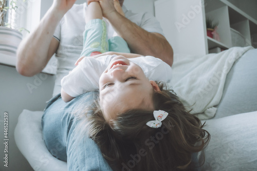 Dad and little girl 2-4 play on the couch. Kid lies on father's lap with her head down, and laughs