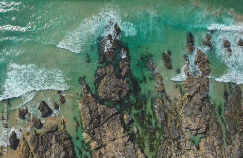 Overhead drone shot of rocky beach with clear blue sea 