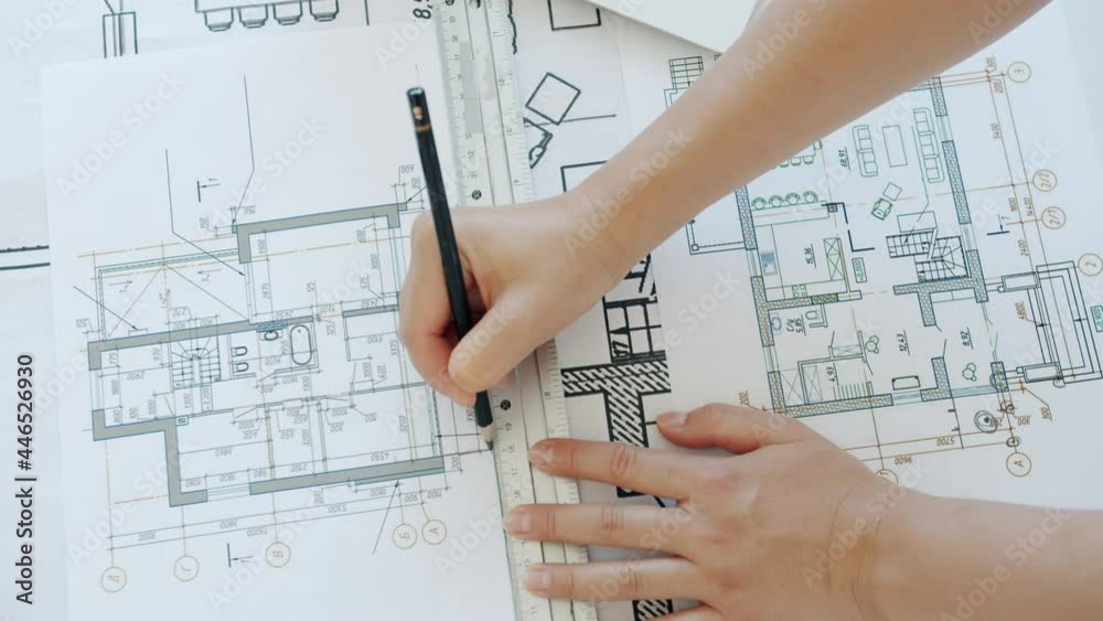 Top view of female hands architect drawing building plan with pencil concentrated on blueprint. Professionals at work and business activities concept.
