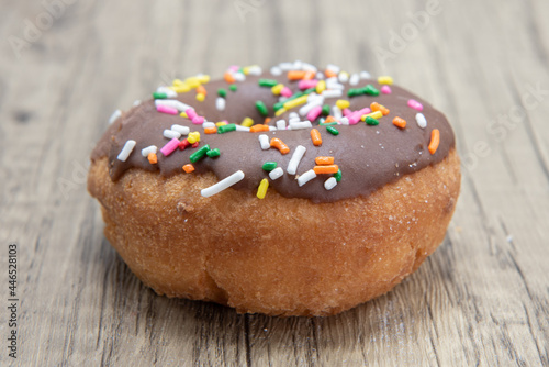 Overhead view of chocolate raised donut is textured with colored sprinkles coating for a sweet treat delight