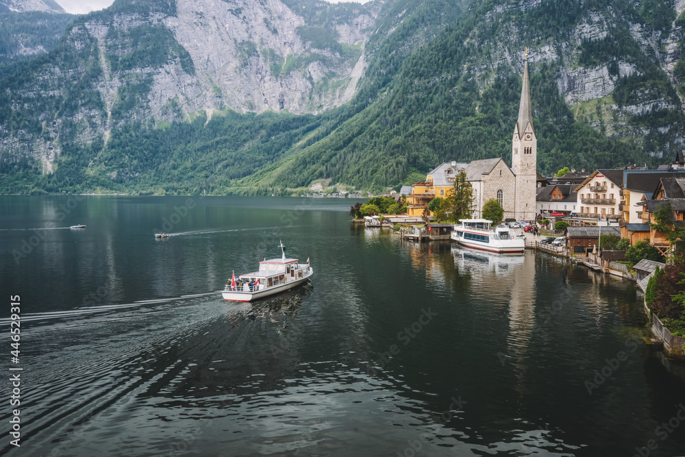 Mountain lake and tourist boat reaching Hallstatt village with Alps in background. Austria