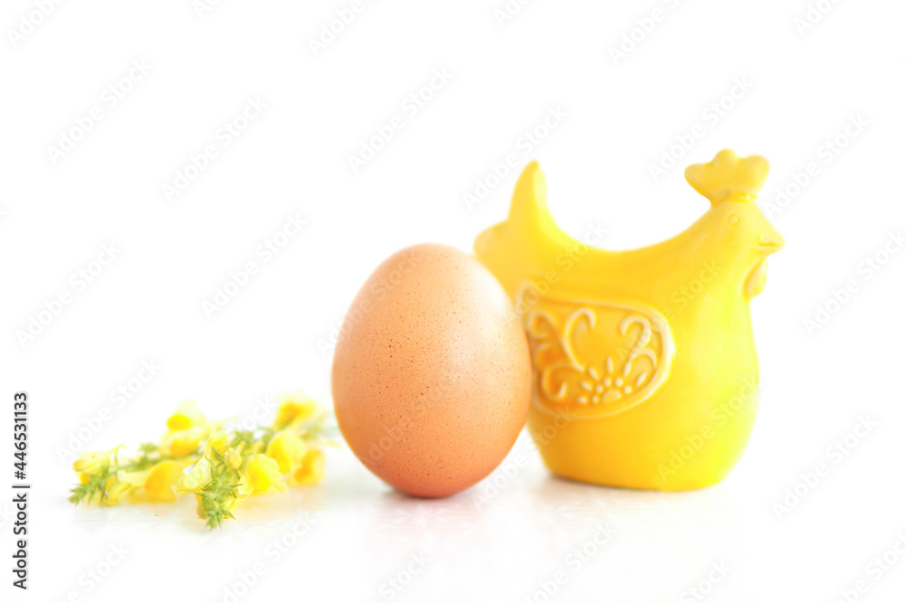 a yellow ceramic figurine of a hen, a brown hen's egg and yellow wildflowers. isolate on a white background. green farming concept.. a yellow ceramic figurine of a hen, a brown hen's egg and yellow wildflowers. isolate on a white background. green farming concept..