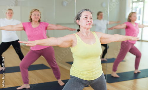 Active elderly woman practicing stretching yoga postures on mat at group class