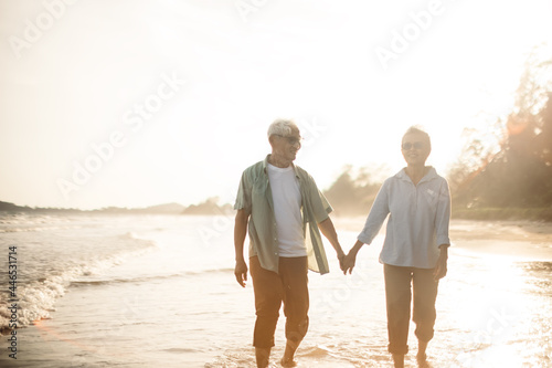 Romantic Senior couple strolling happily along the beach in the sunshine sunset. Retirement concept and happy life.