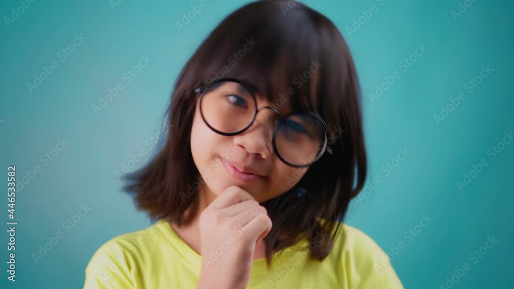 Portrait young Asian girl wearing glasses thinking, cute Thai student looking camera on blue background Portrait young Asian girl wearing glasses thinking, cute Thai student looking camera on blue background