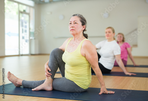 Senior woman maintaining mental and physical health attending group yoga class at studio, practicing twisting poses