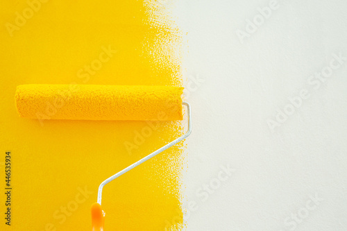 Woman roller paints yellow on the wall of the house herself for savings.