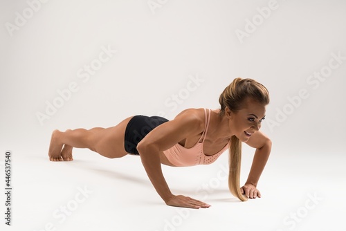 Smiling sporty woman doing push ups exercise in studio