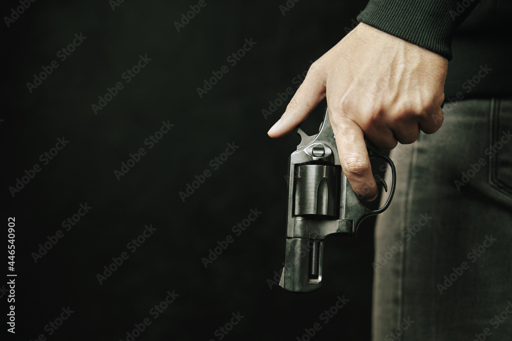 Guy with gun down. Black revolver with drum in man's hand. Armed person on dark background. Firearms for attack or defense. Guy with gun down. Black revolver with drum in man's hand. Armed person on dark background. Firearms for attack or defense.