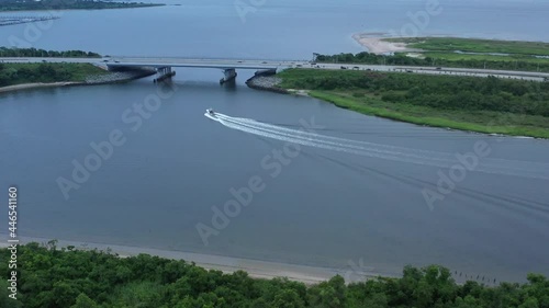 A high angle drone shot of a boat speeding in Gerritsen Creek on a cloudy morning. The drone camera dolly in, following the boat as it speeds to go under the Belt Parkway. photo