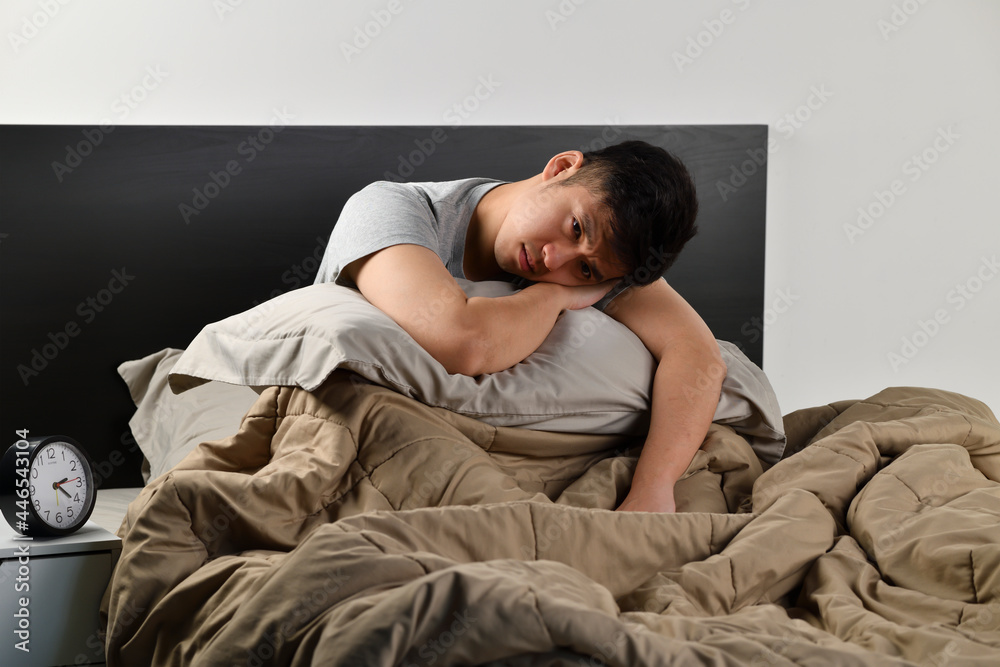 Depressed young Asian man sitting in bed cannot sleep from insomnia Depressed young Asian man sitting in bed cannot sleep from insomnia