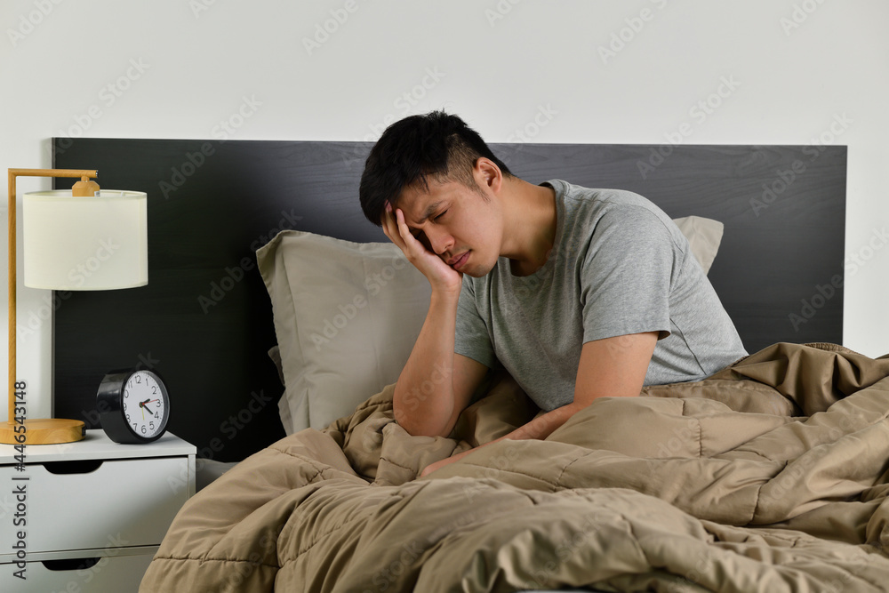 Depressed young Asian man sitting in bed cannot sleep from insomnia Depressed young Asian man sitting in bed cannot sleep from insomnia