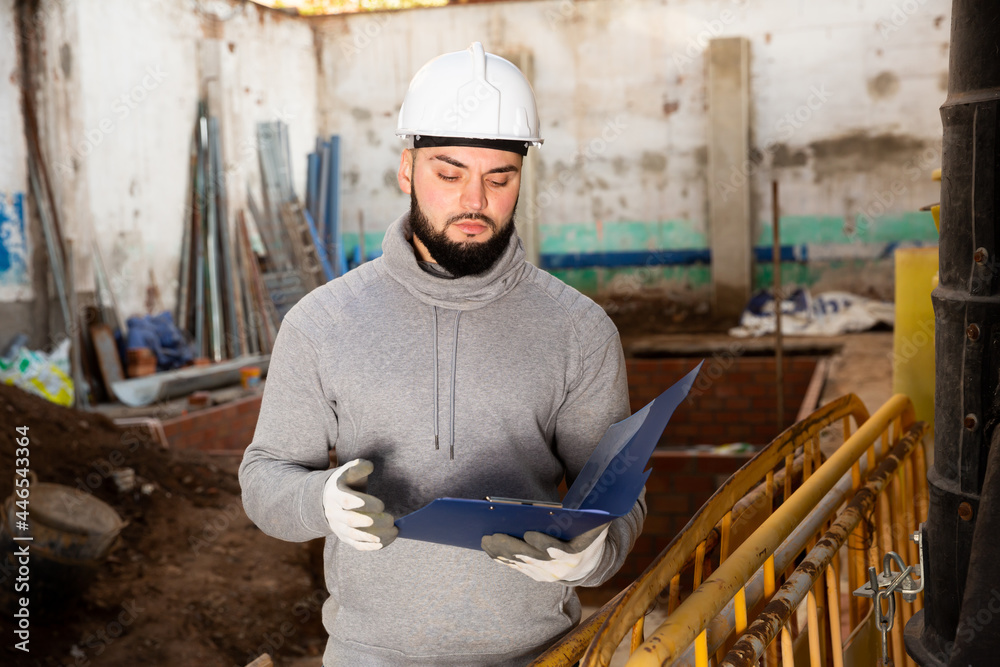 Fototapeta premium Confident young supervisor inspecting process of building overhaul, comparing to blueprints