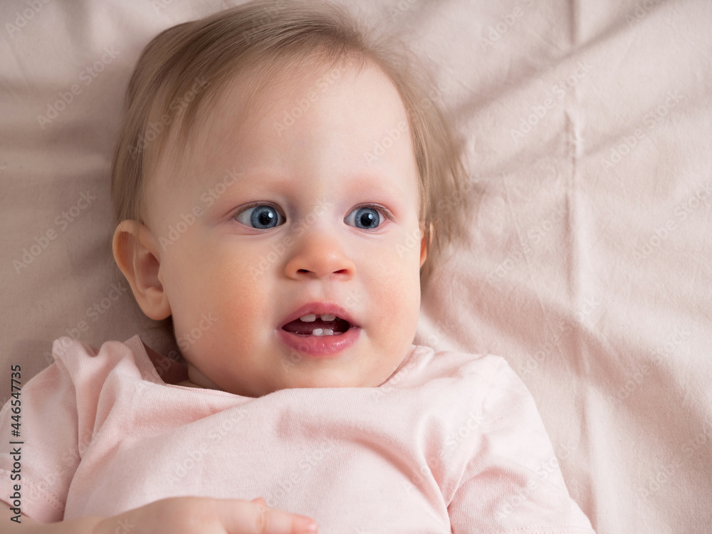 Little baby girl looks away in surprise, close-up. Portrait of a beautiful light girl in pink tones. Child age one year
