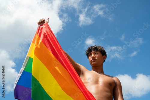 Portrait of young Hispanic gay boy looking at camera  holding LGBT flag - Focus on face landscape imagin