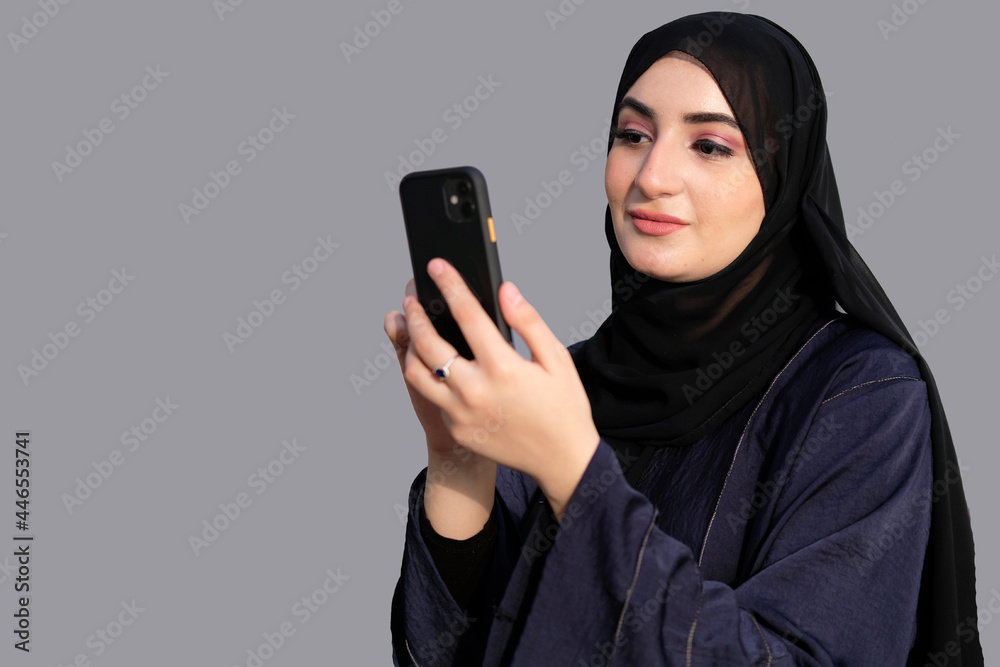 Arab in Abaya using cellphone ideal for mobile app or online banking concept. Woman on traditional UAE Emirati clothing Arab in Abaya using cellphone ideal for mobile app or online banking concept. Woman on traditional UAE Emirati clothing