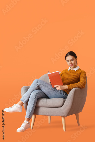 Beautiful young woman with book sitting in armchair on color background © Pixel-Shot