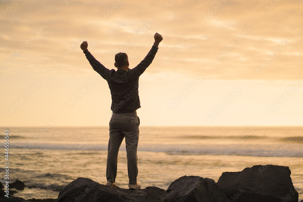Fototapeta premium happy successful MAN in YES POSE on beach rocks AT THE ocean WITH arms wide open enjoying life 