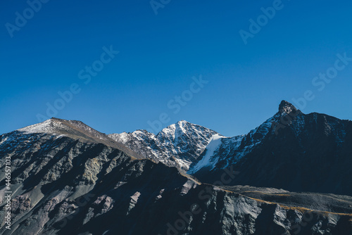 Fototapeta Naklejka Na Ścianę i Meble -  Atmospheric mountain landscape with dark mountains silhouettes. Sharp rocky pinnacle and snow-covered top in sunlight. Alpine scenery with black orange mountain with peaked top in sunshine in autumn.