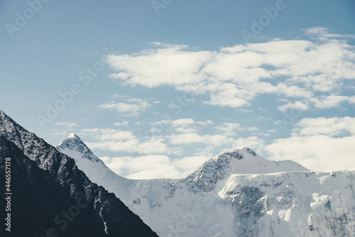 Minimalist alpine landscape with high snow-covered mountain with snowy peaked top under cirrus clouds. Beautiful mountain scenery with great snow-white sharp pinnacle in cloudy sky. Awesome mountains.