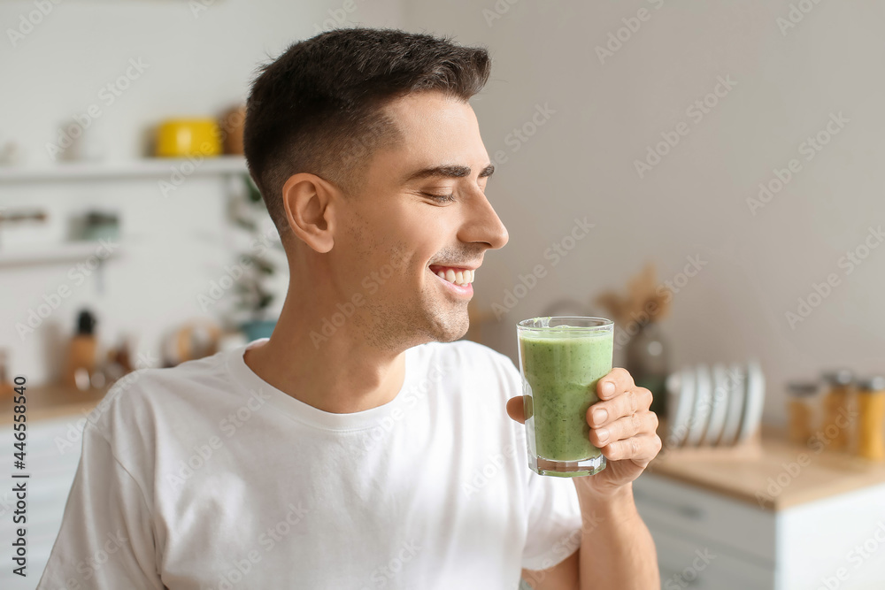 Young man drinking healthy green smoothie in kitchen